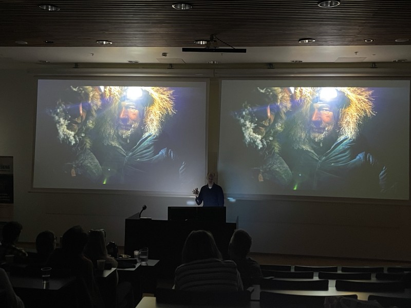 Auditorium og to identiske skjermar, der mann held foredrag. Motiv på skjerm: mann i polarutstyr med rim i skjegget, hette og hovudlykt