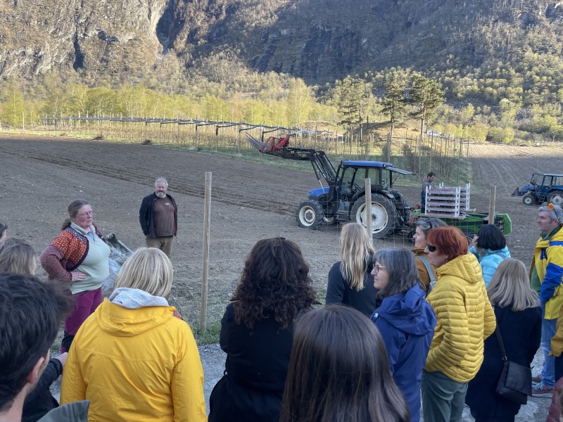 To bønder på åker med traktor snakkar til folk i allversklede på ekskursjon