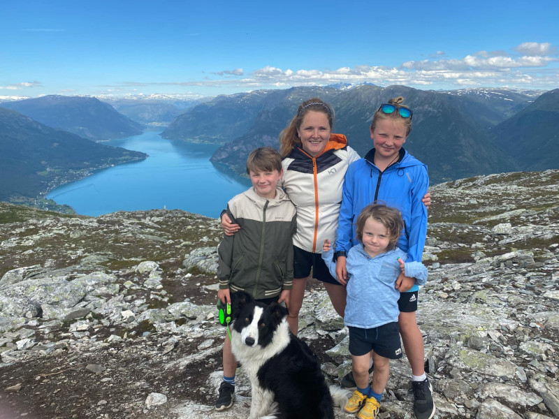 Mor med søner og hund på topp i fjell- og fjordlandskap