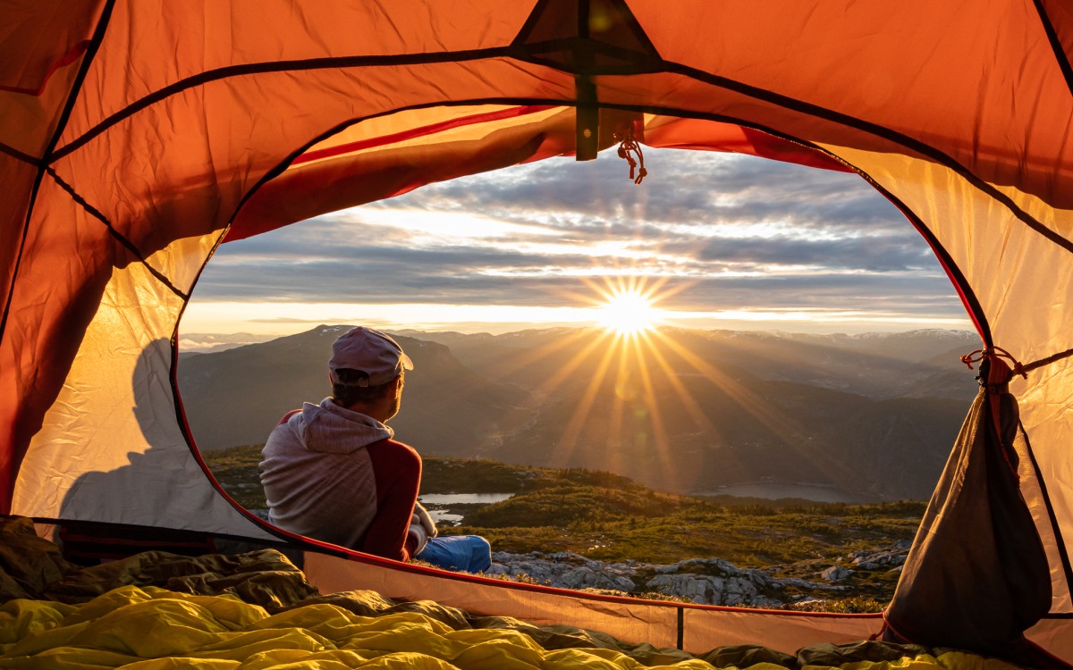 Teltopning med person og sol i horisonten