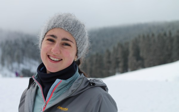 jente med ullhue og anorakk i landskap med snø og skog. smiler til kamera