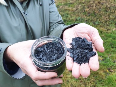 Hand som held behaldar med biokol og ei anna hand med litt av innhaldet.