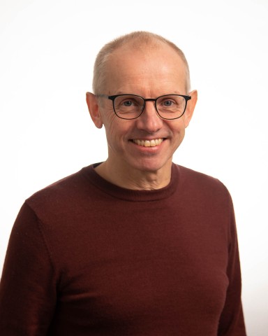 middelaldrande mann med raudbrun genser og briller, smiler