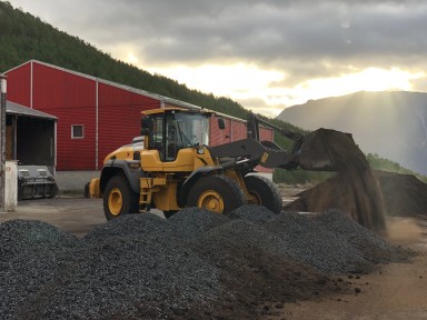 Traktor på avfallsplass med haug av svart biokol framfor seg