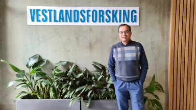 Middelaldrande mann står framfor inngangsparti med logoen "Vestlandsforsking" og potteplanter i hoftehøgde bak.