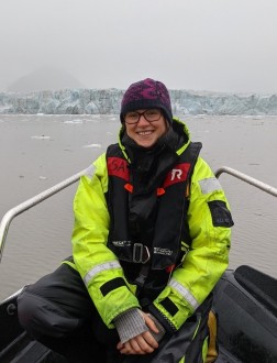 Kvinne på RIB-båt ved isbre og fjord med isflak. Godt kledd, smiler til kamera.