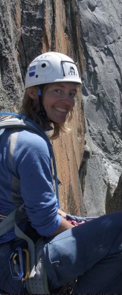 Kvinne i klatrehjelm ved fjellvegg, smiler